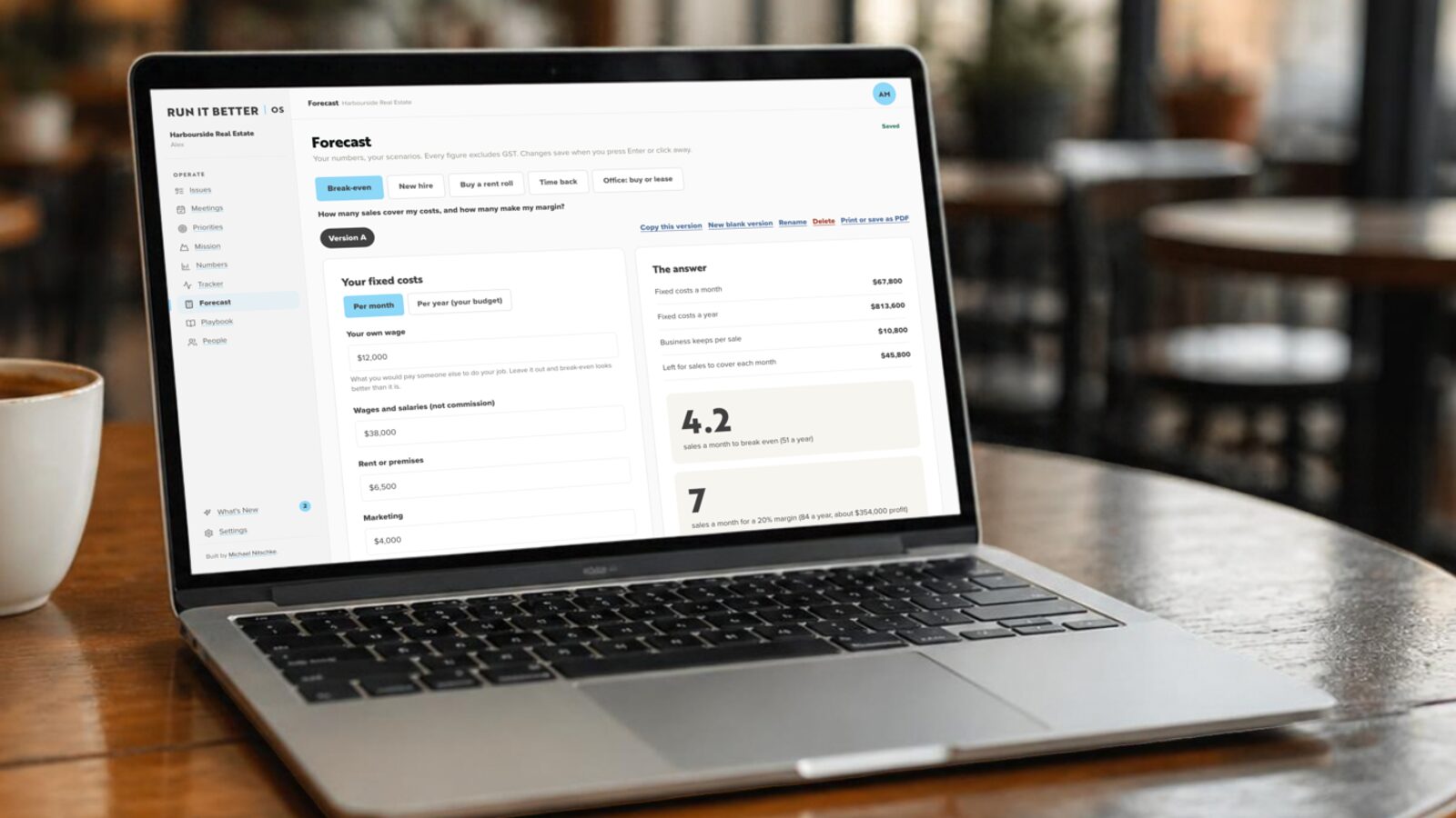 Run It Better OS on a laptop in a cafe, showing a break-even forecast